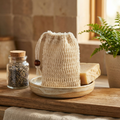 Sisal Bag with drawstring and wooden bead on a ceramic dish next to natural soap and plant in soft light