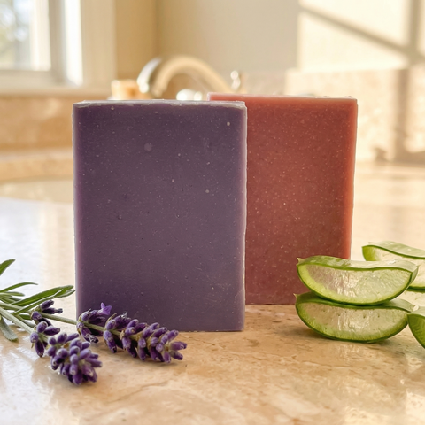 Two bars of Oatmeal & Aloe | Lavender & Goats Milk soap with lavender flowers and aloe slices on a marble surface