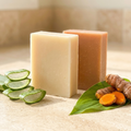 Two natural bars of Aloe Vera & Calendula | Turmeric Soap with sliced aloe vera and fresh turmeric on leaves.