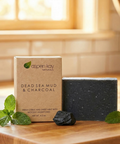 Dead Sea Mud & Charcoal - Bar Soap displayed with fresh mint leaves and charcoal on a wooden surface.