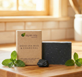 Dead Sea Mud & Charcoal - Bar Soap displayed with fresh mint leaves and charcoal on a wooden surface.