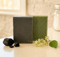 Dead Sea Mud & Charcoal | Neem & Dead Sea Mud natural bar soaps with charcoal pieces and neem flowers on a smooth surface